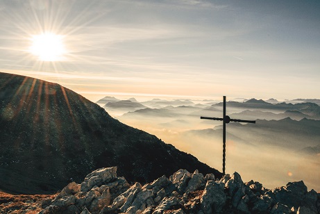 Atop a mountain range, a cross is illuminated in the light of the sun.